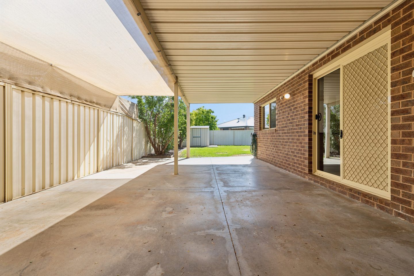 Long covered patio beside the brick home, opening to the rear lawn